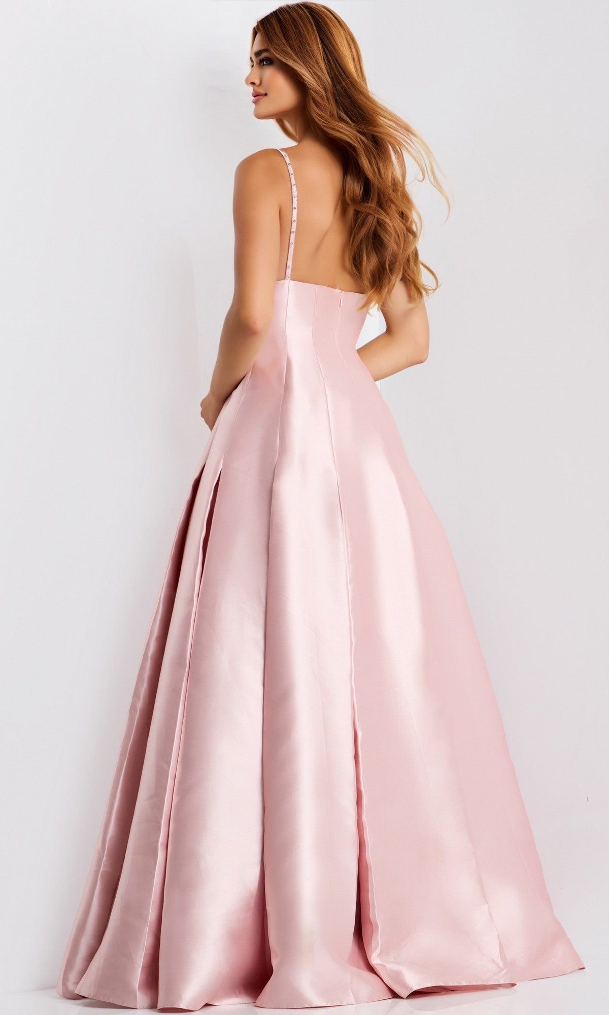 A woman models the Jovani 48732 long prom dress: a floor-length light pink satin A-line gown with thin straps, an open back, and a beaded bodice, posed against a plain background.